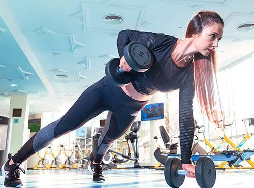 Young-brunette-girl-holding-a-plank-while-lifiting-weights-at-a-gym
